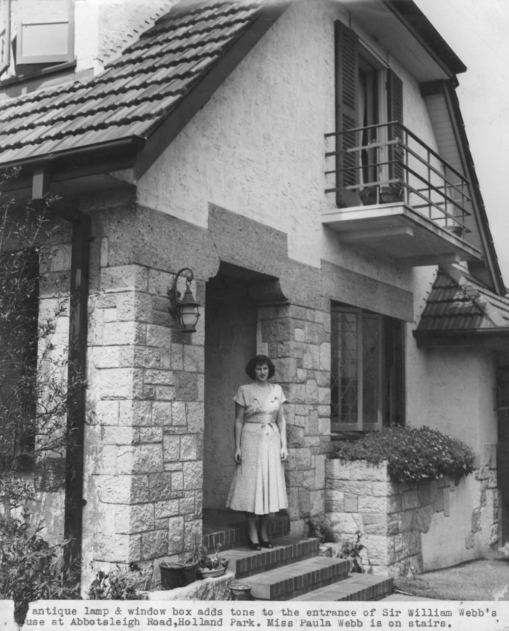 This is an image of the Front entrance to the Webb family residence in Holland Park, 1948. the caption reads "antique lamp & window box adds tone to the entrance of Sir William Webb's house at Abbotsleigh Road, Holland Park. Miss Paula Webb is on stairs"