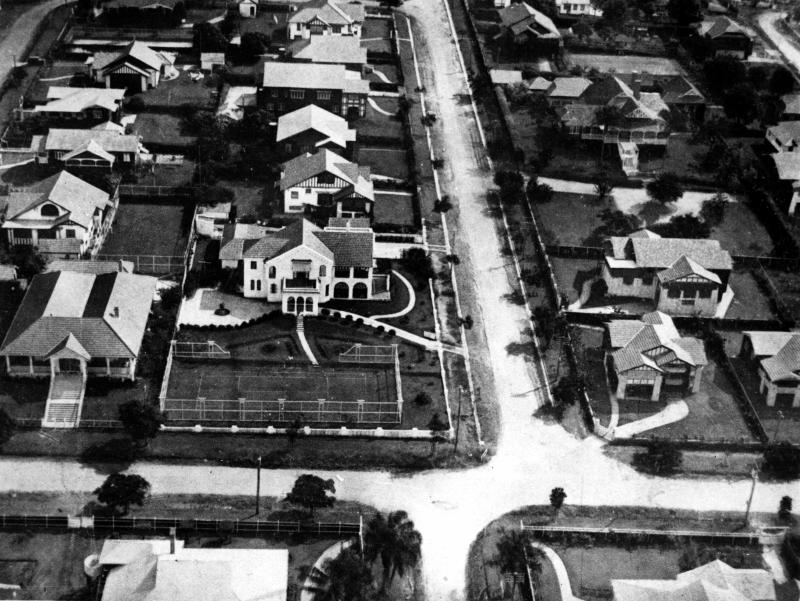 This is an image of ‘Aerial view of houses in Clayfield, Brisbane, 1930’, viewed from the intersection of Enderley and Alexandra roads, Clayfield, looking west.