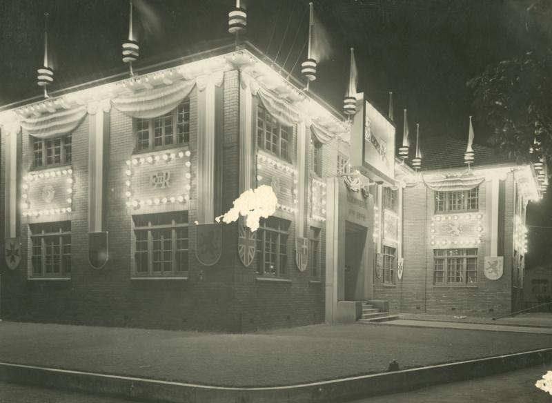 This is an image of 'Hornibrook House lit up for the Queen's visit in Newstead, Queensland, 1954', viewed from the corner of Breakfast Creek Road & Newstead Avenue, Newstead, looking south-east.
